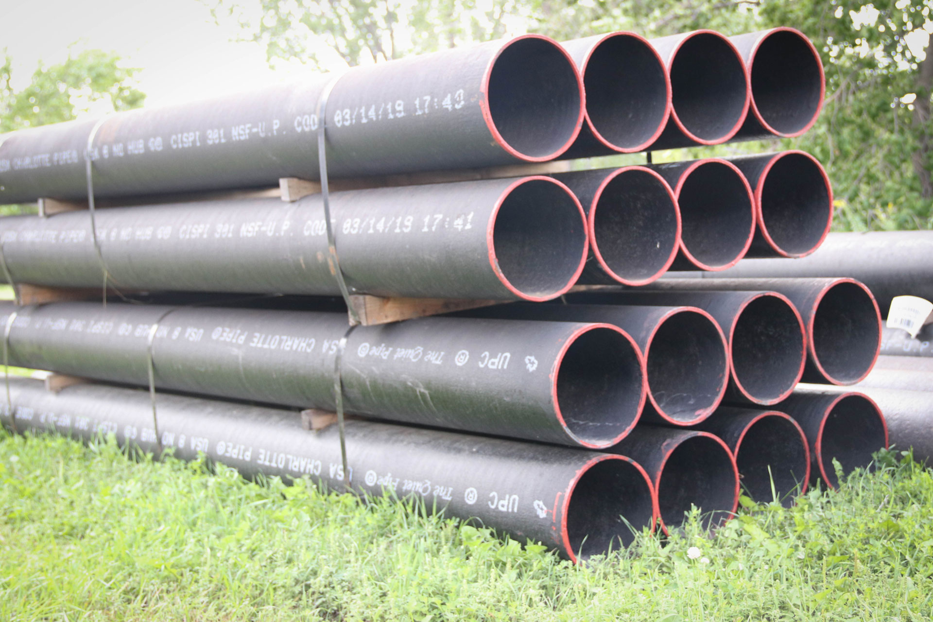 Stacked black pipes outdoors on grass.